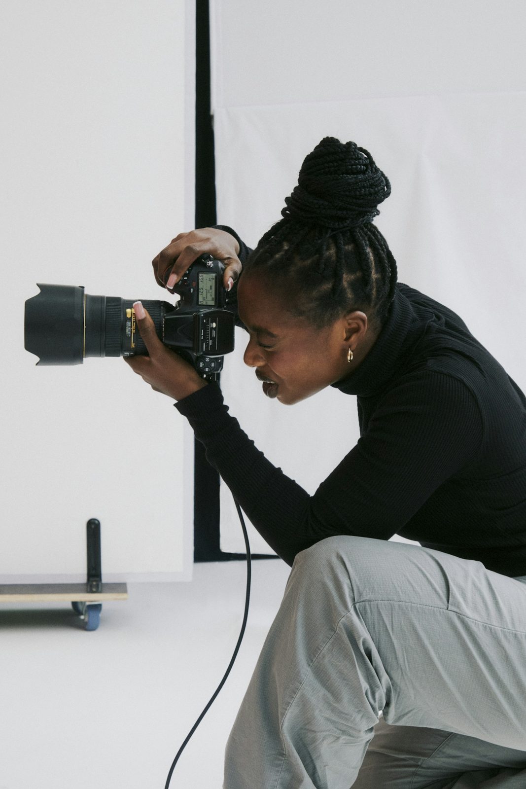 A photographer crouched behind a camera on a tripod in a bright white studio