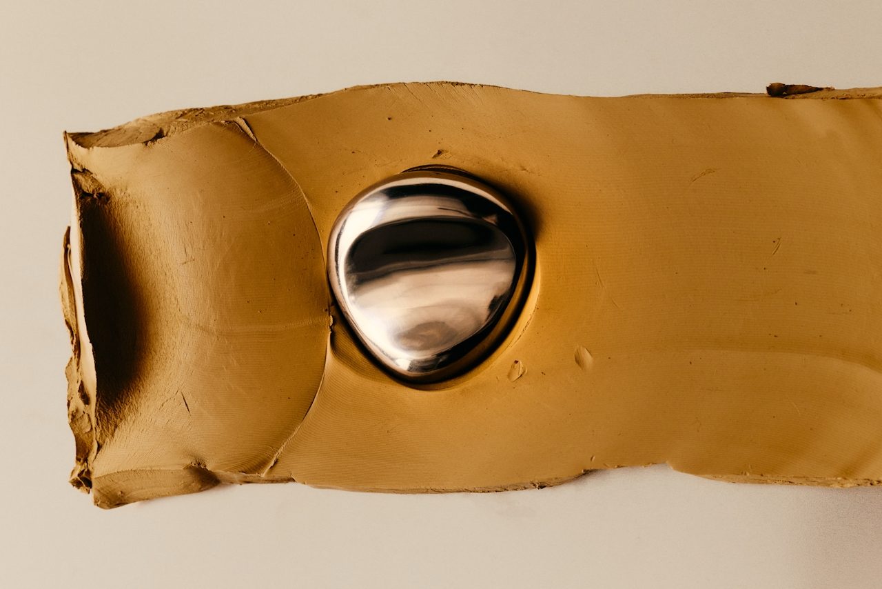 A smear of ochre clay on a pale surface with a polished metal pebble pressed into it