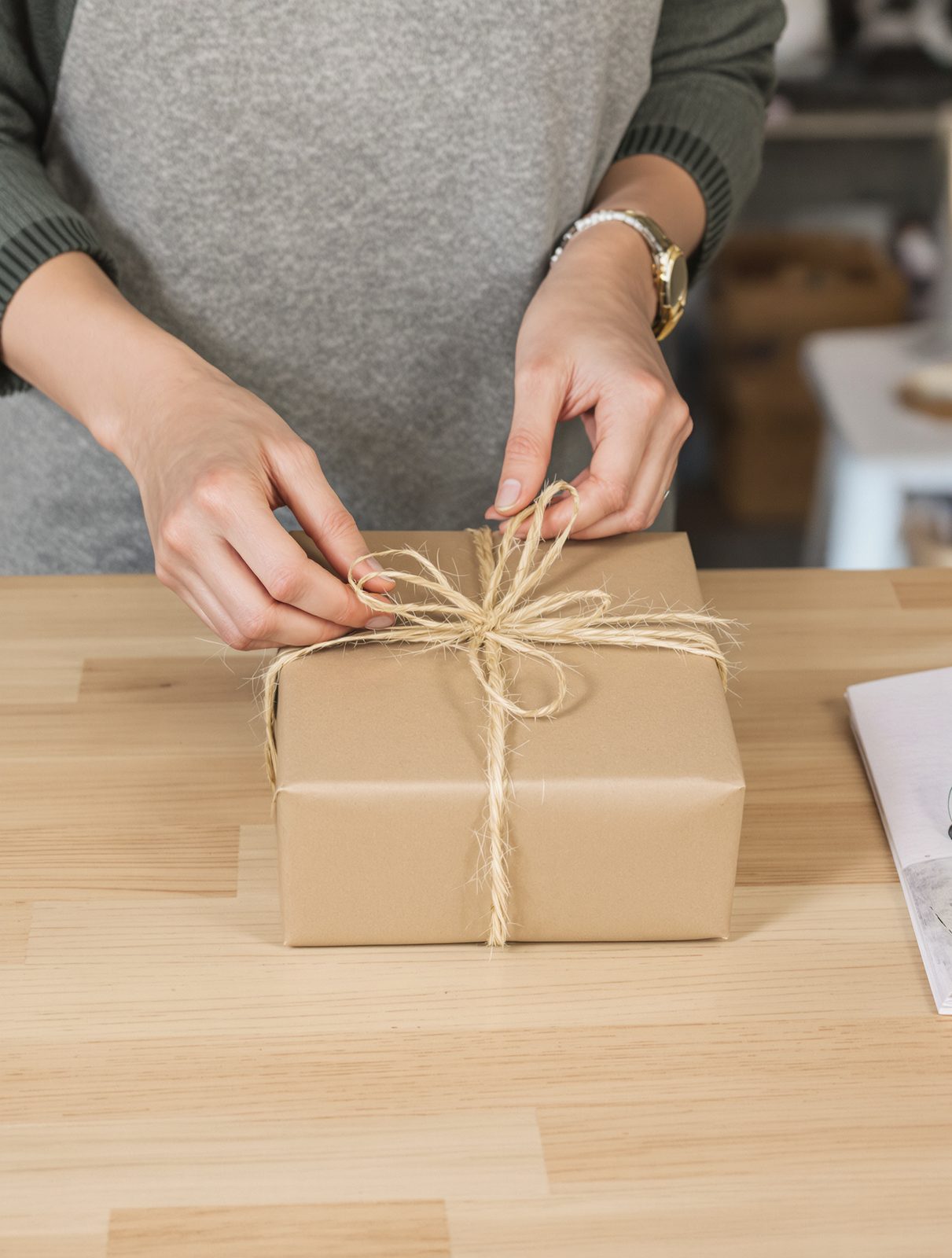 Hands tying twine around a kraft-paper parcel, an order being packed to ship